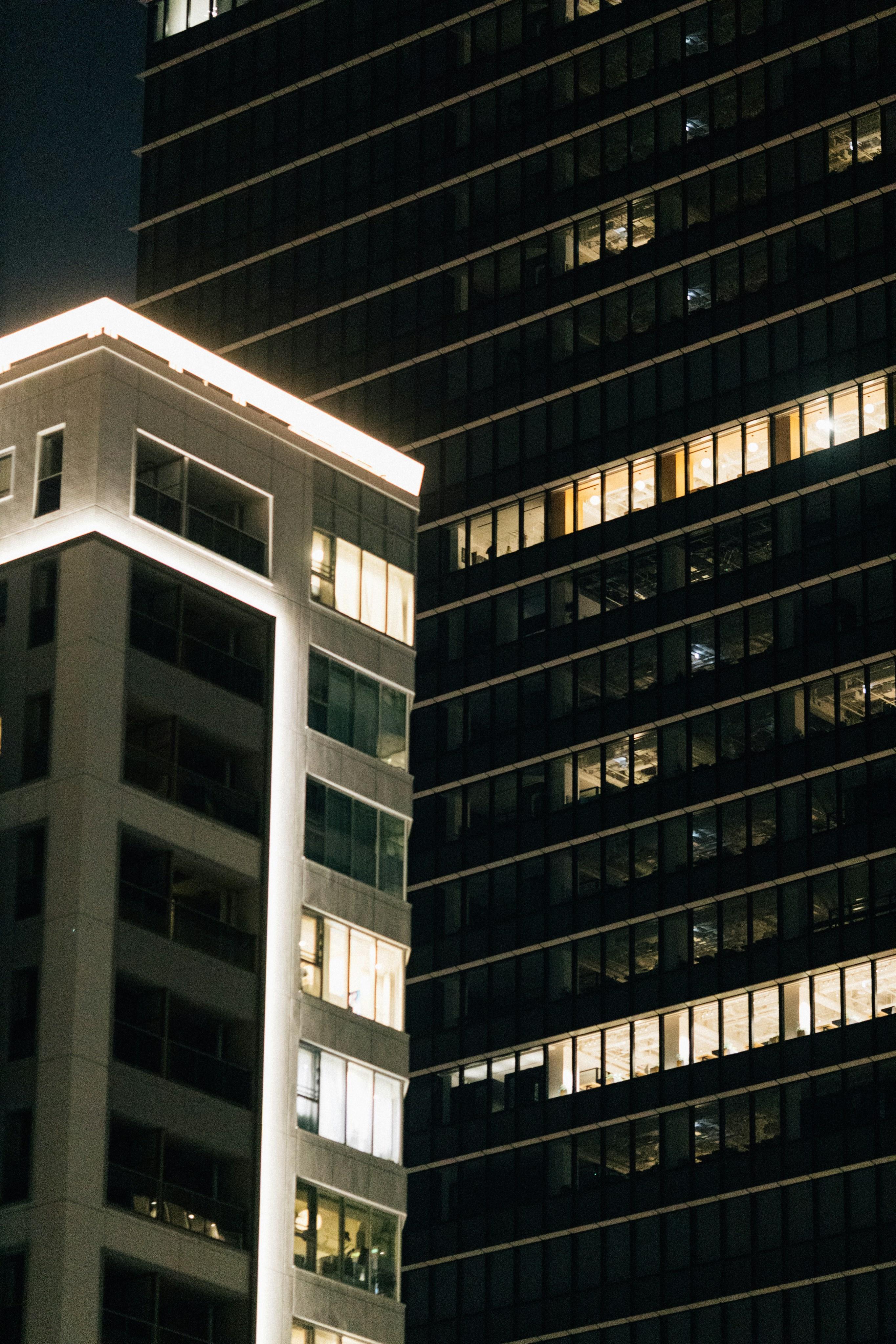 Dark high-rise towers at night with scattered, warmly lit windows against a navy sky.